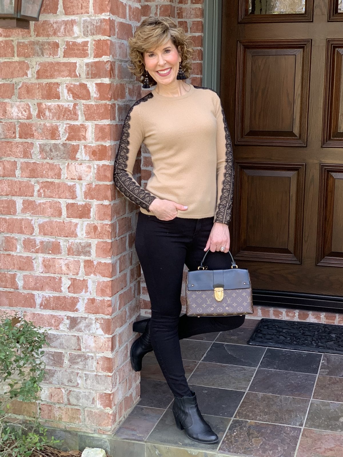 woman standing in archway wearing tan sweater and black pants