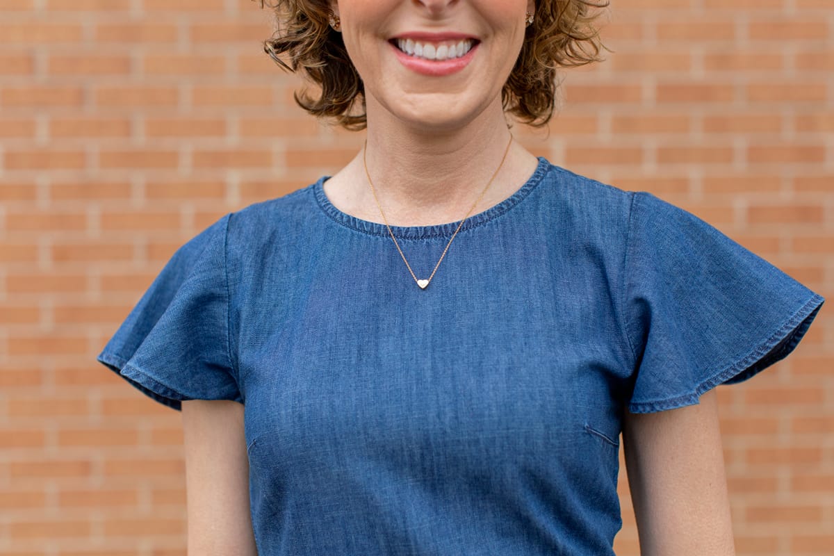 woman from lips down to waist wearing blue with heart necklace