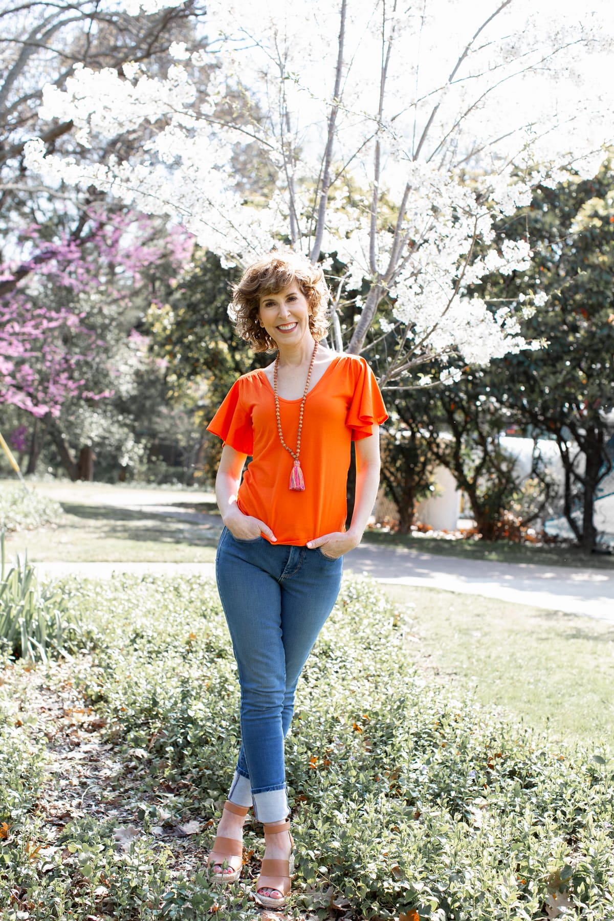 woman in orange shirt and tassel necklace in park