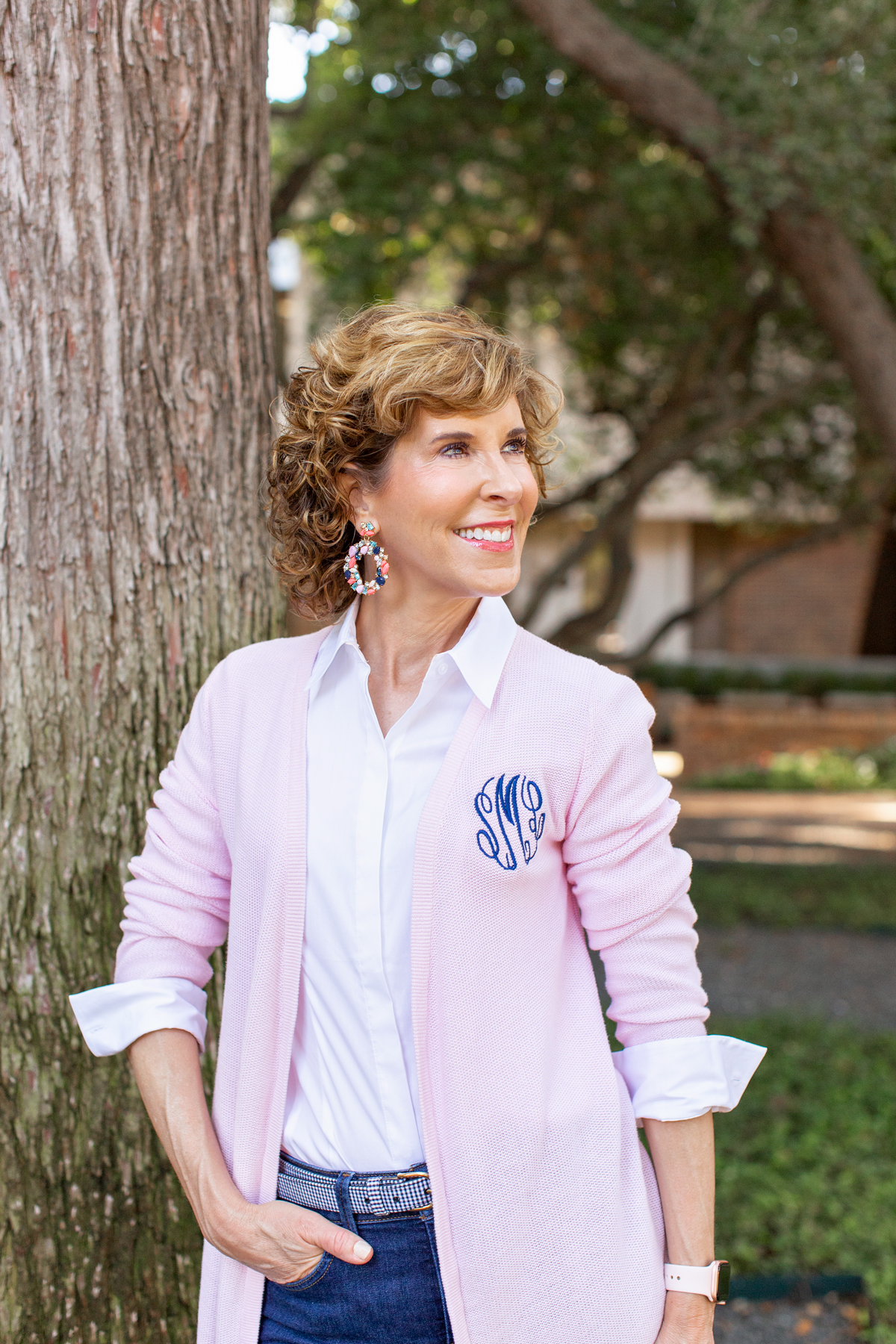 woman in pink cardigan standing next to a tree trunk looking to the side