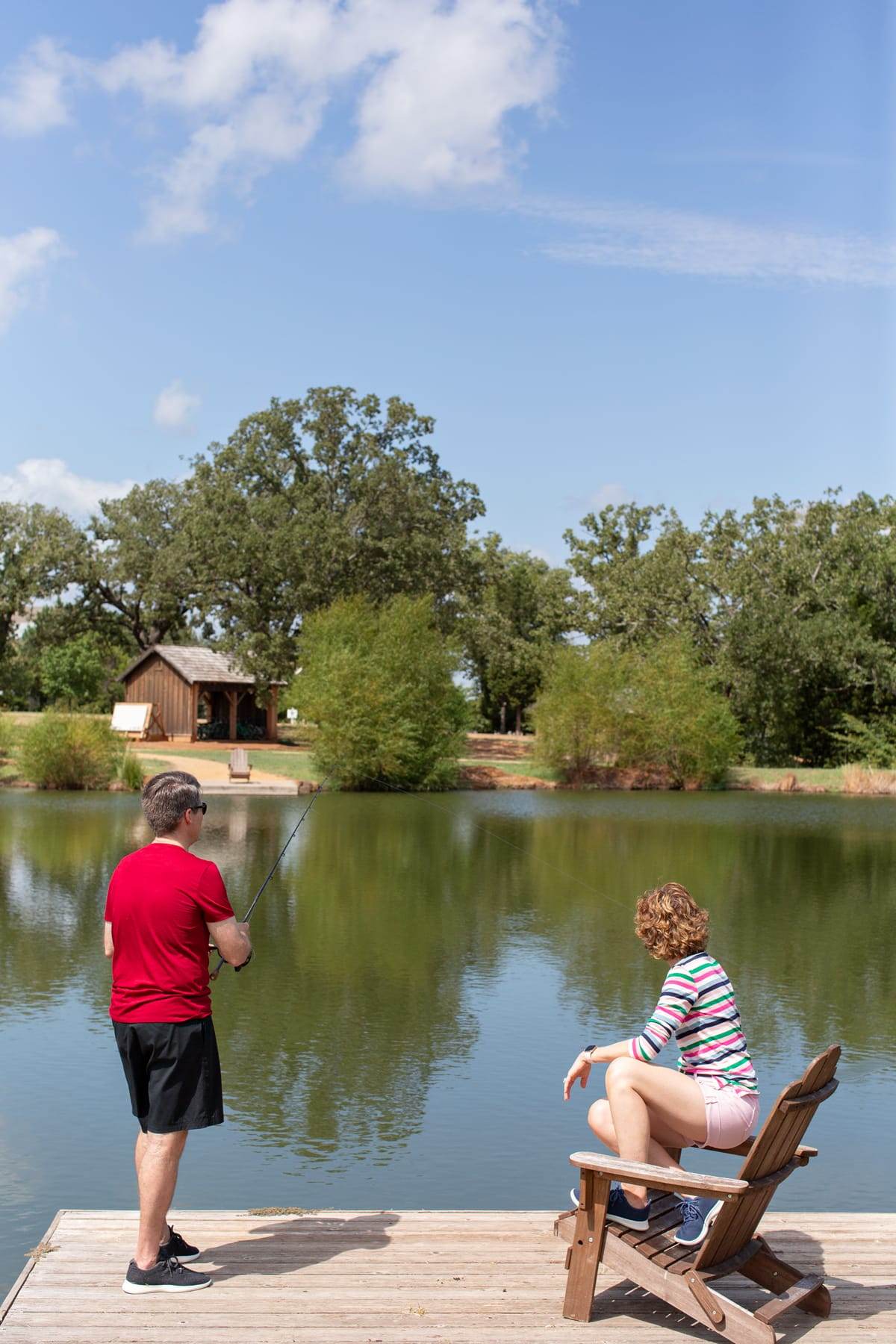 a woman watching a man fishing on a lakeside dock at long cove