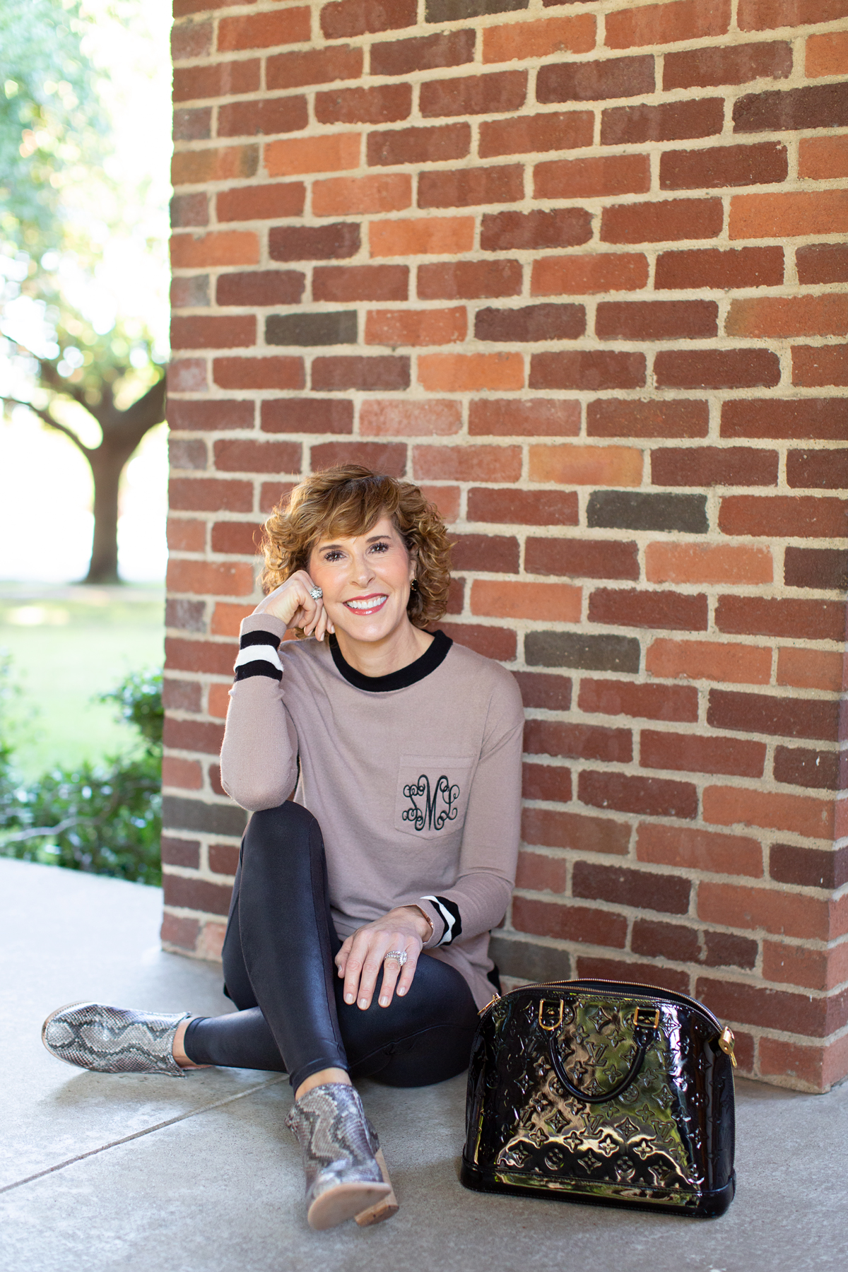 woman in tan monogrammed sweater sitting in front of a brick wall