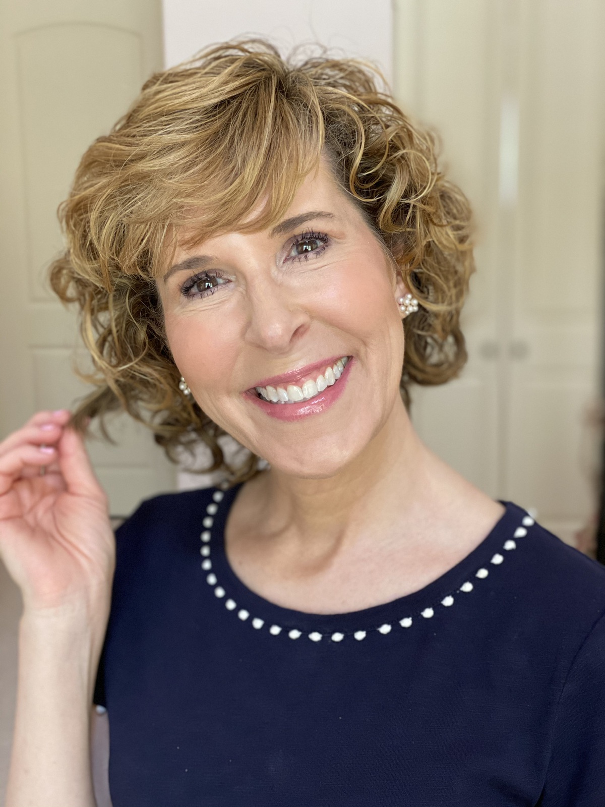 woman in navy blue top smiling into the camera and touching her hair