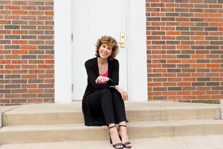 woman sitting in front of doorway in pink top with black sweater