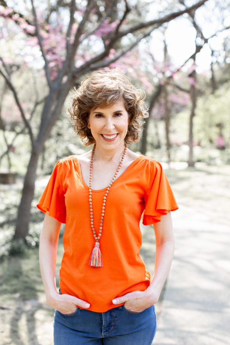 woman in orange shirt and tassel necklace in park