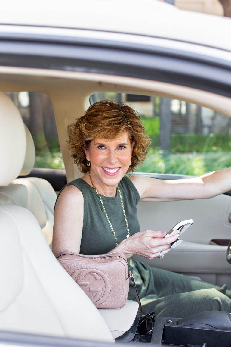 woman in green dress sitting in her car holding her phone looking at camera and reviewing the new rules for texting