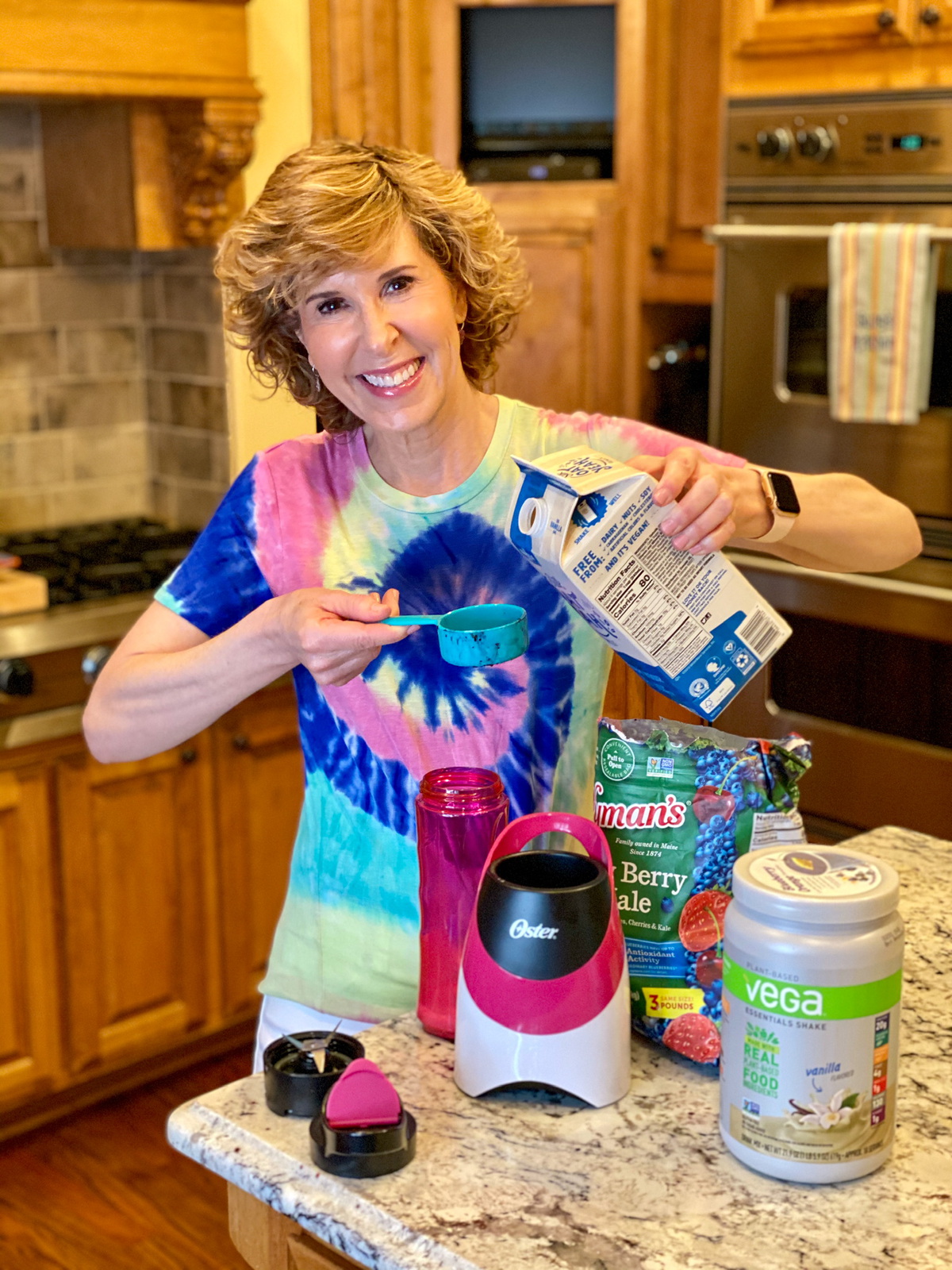 woman in tie dye shirt making a smoothie in kitchen