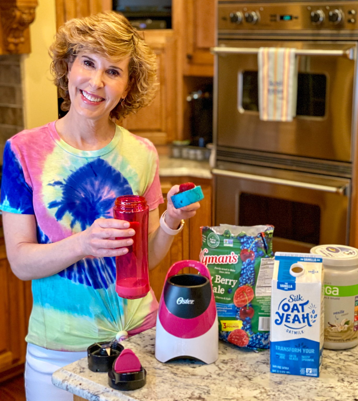 woman in tie dye shirt making a smoothie in kitchen