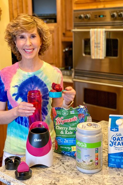 woman in tie dye shirt making a smoothie in kitchen