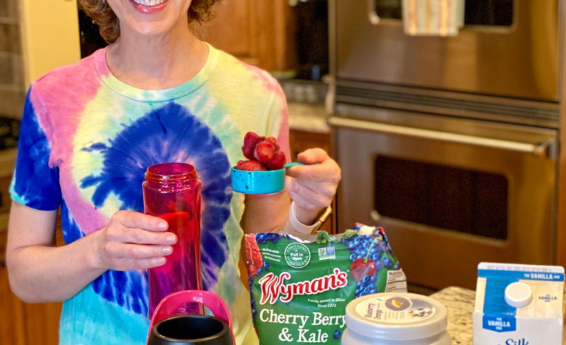 woman in tie dye shirt making a smoothie in kitchen