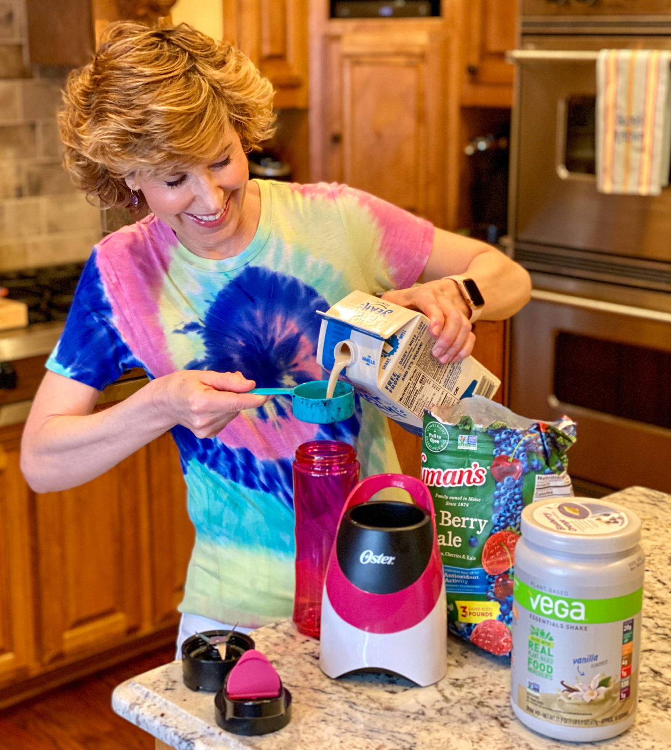 woman in tie dye shirt making a smoothie in kitchen