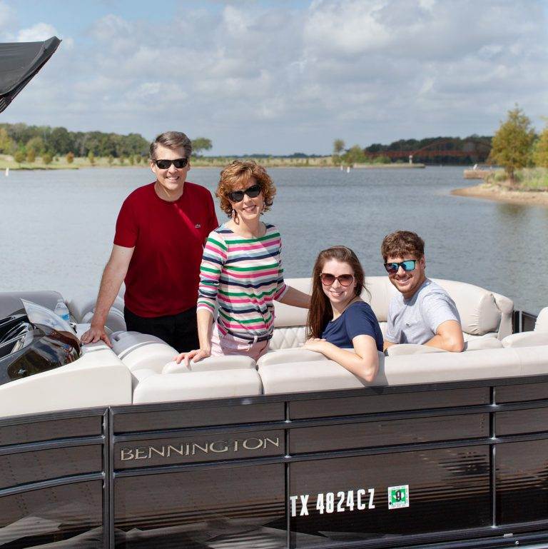 a family of four on a boat looking at camera with a lake behind them