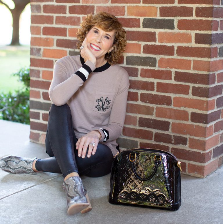 woman in tan monogrammed sweater sitting in front of a brick wall