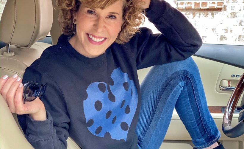 woman sitting in car with one leg up on her seat wearing black sweatshirt with blue polka dot heart sweatshirt