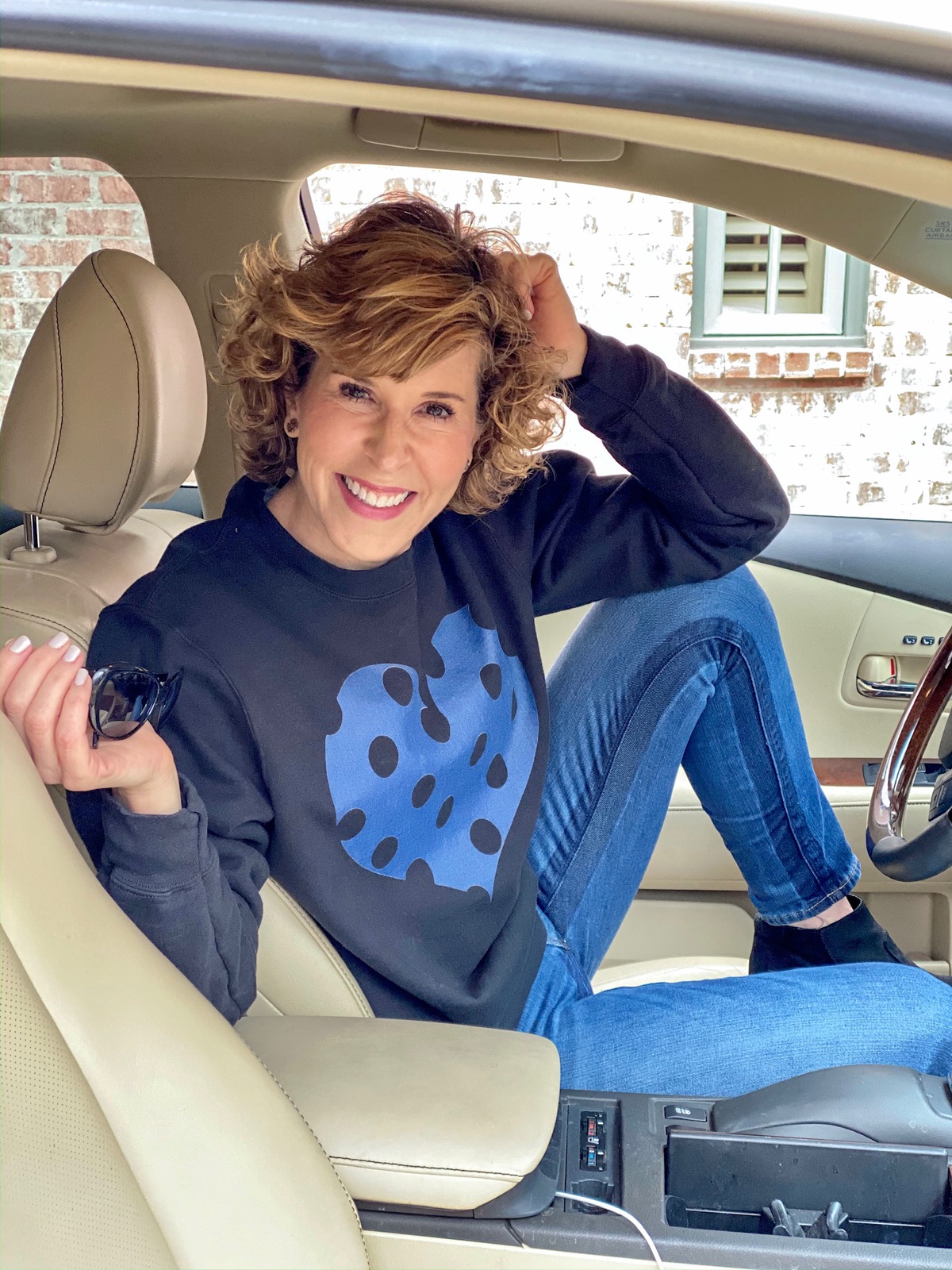 woman sitting in car with one leg up on her seat wearing black sweatshirt with blue polka dot heart sweatshirt