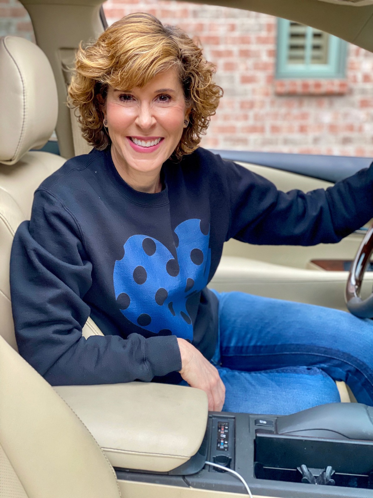 woman sitting in car wearing black sweatshirt with blue polka dot heart