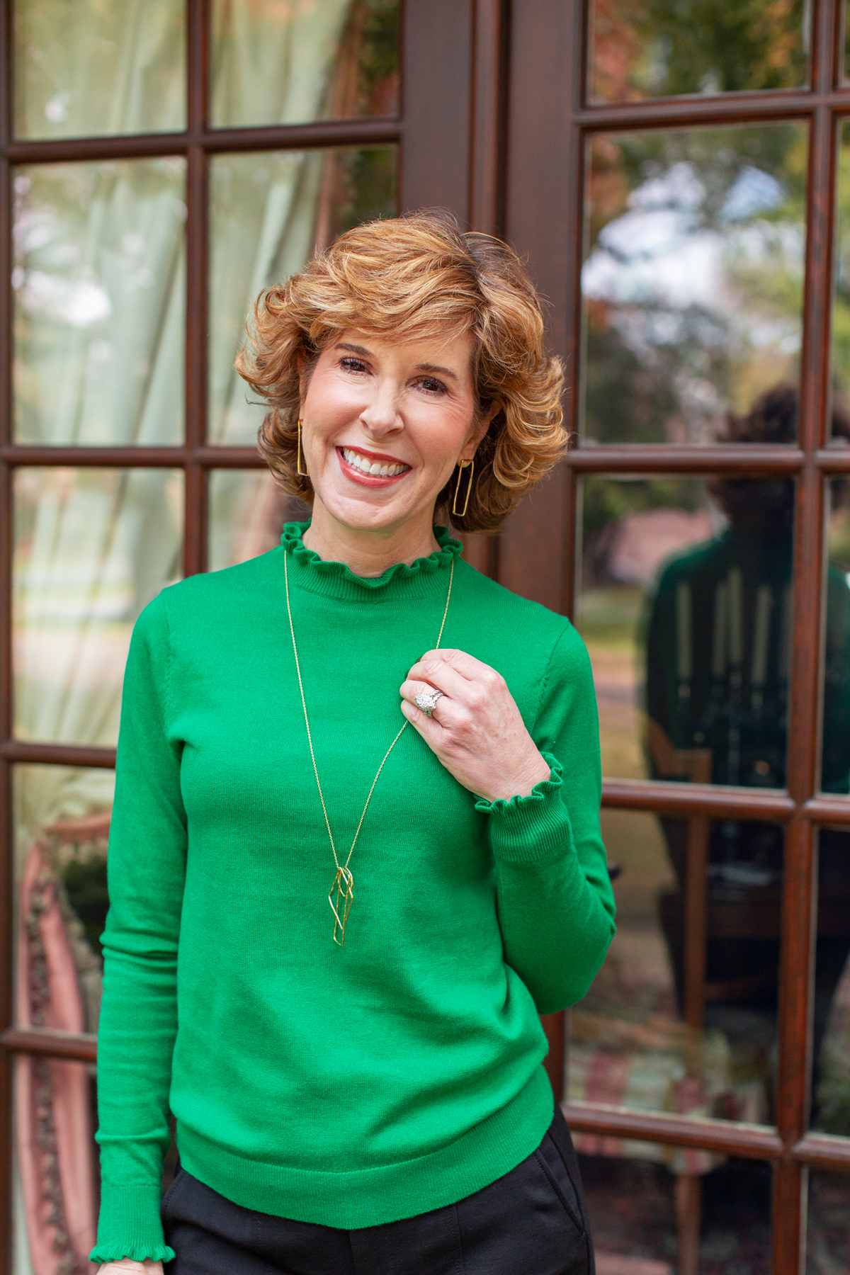 woman in green sweater standing outside a house