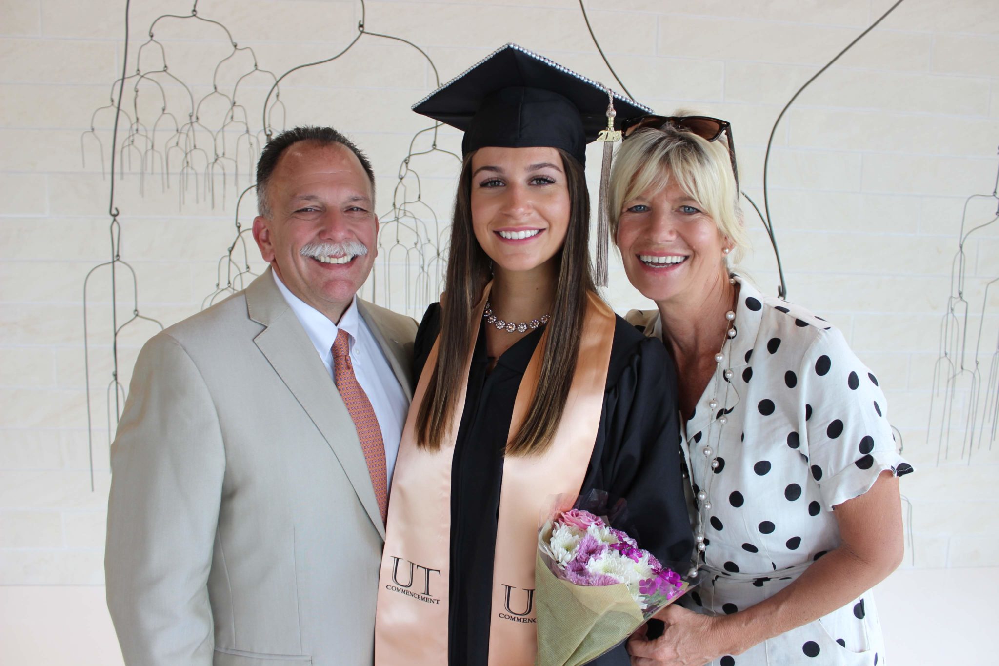 graduation photo of woman in cap and gown with parents on either side