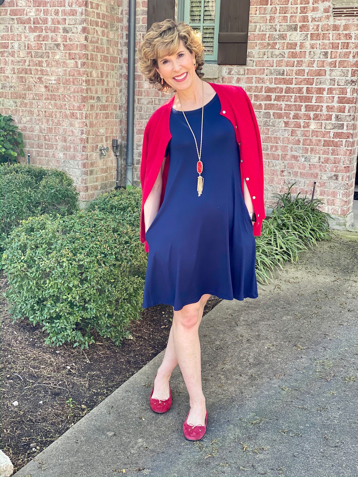 woman wearing blue dress and red cardigan in front of a house