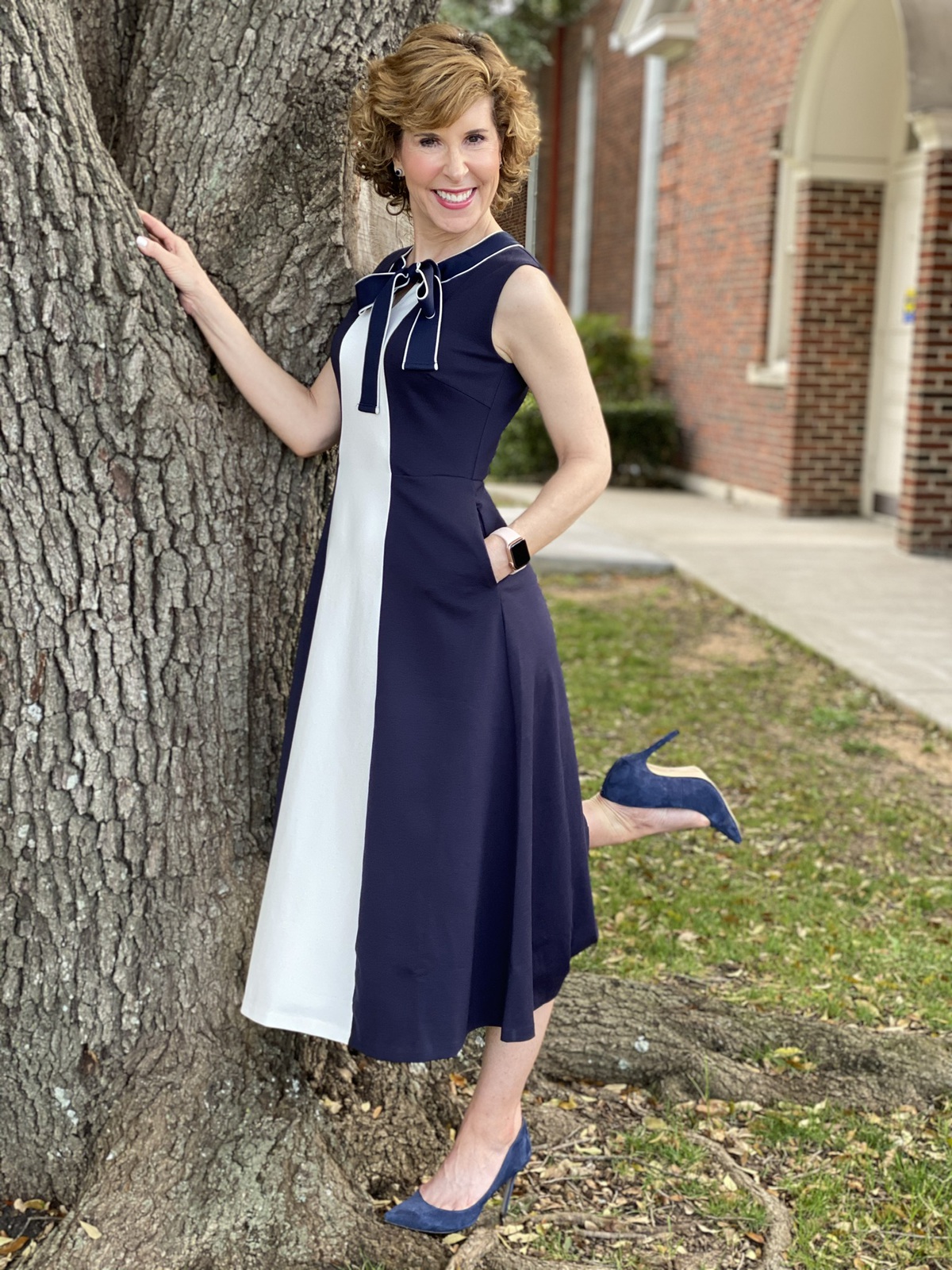woman over 50 wearing navy and cream dress standing by a tree