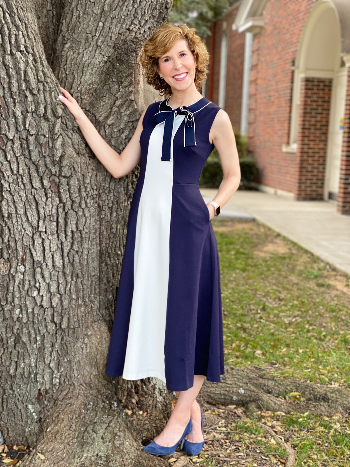 woman over 50 wearing navy and cream dress standing by a tree
