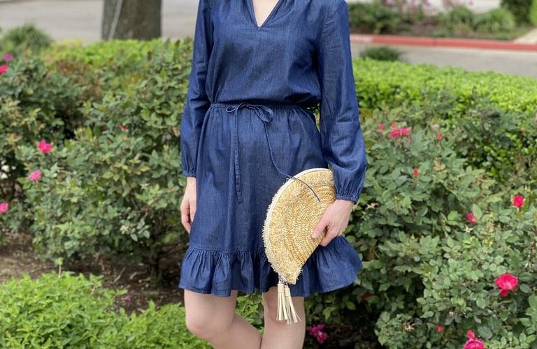 woman wearing chambray draper james popover dress and holding fan clutch straw bag