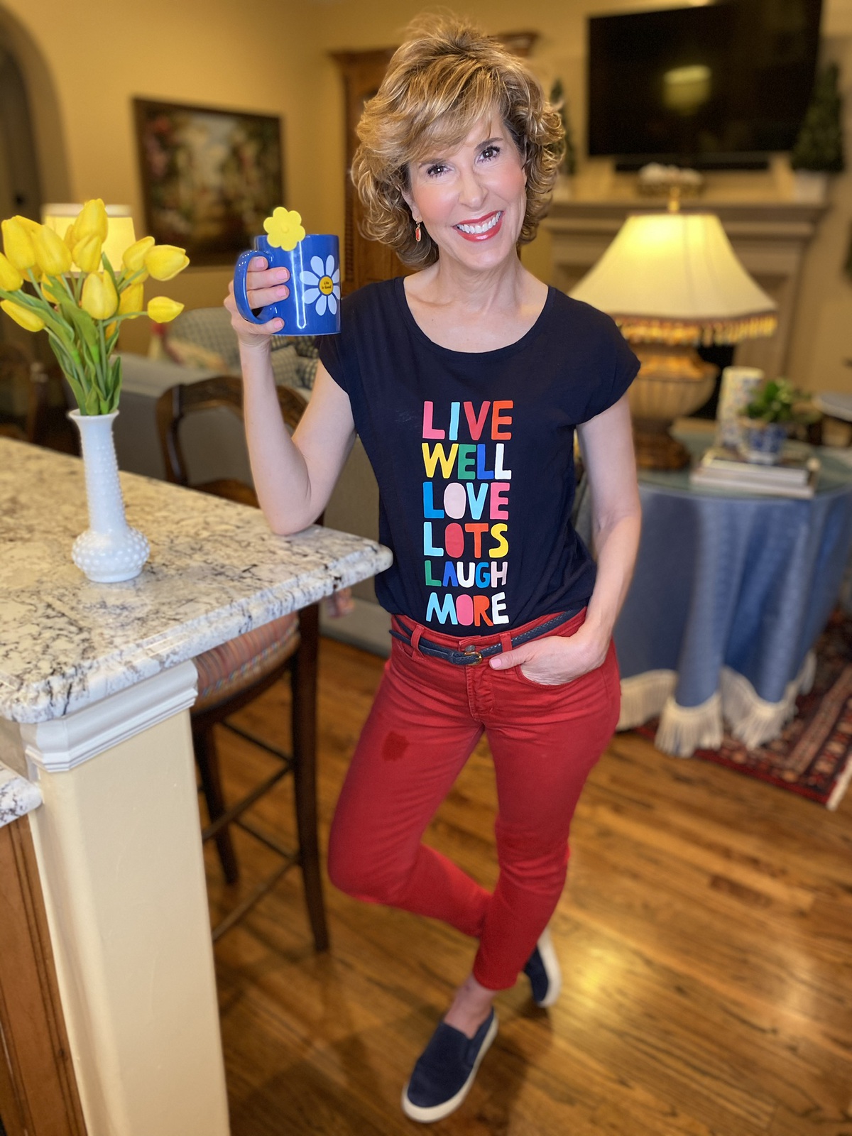 woman wearing navy graphic tee and red jeans drinking tee in her living room