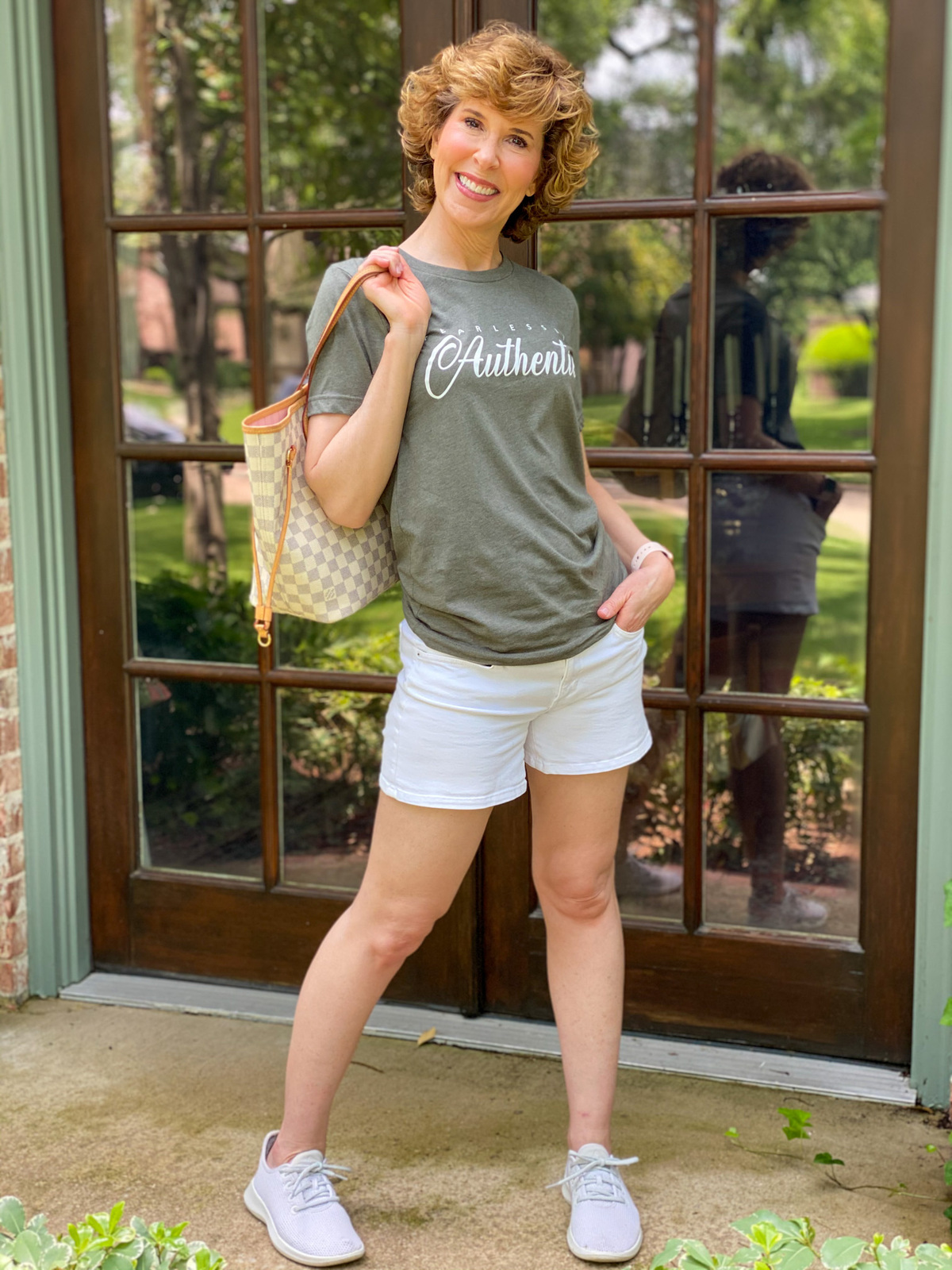 woman over 50 wearing graphic tee standing on porch in front of french doors
