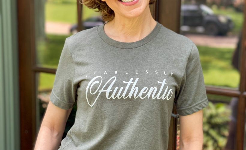 woman over 50 wearing graphic tee standing on porch in front of french doors