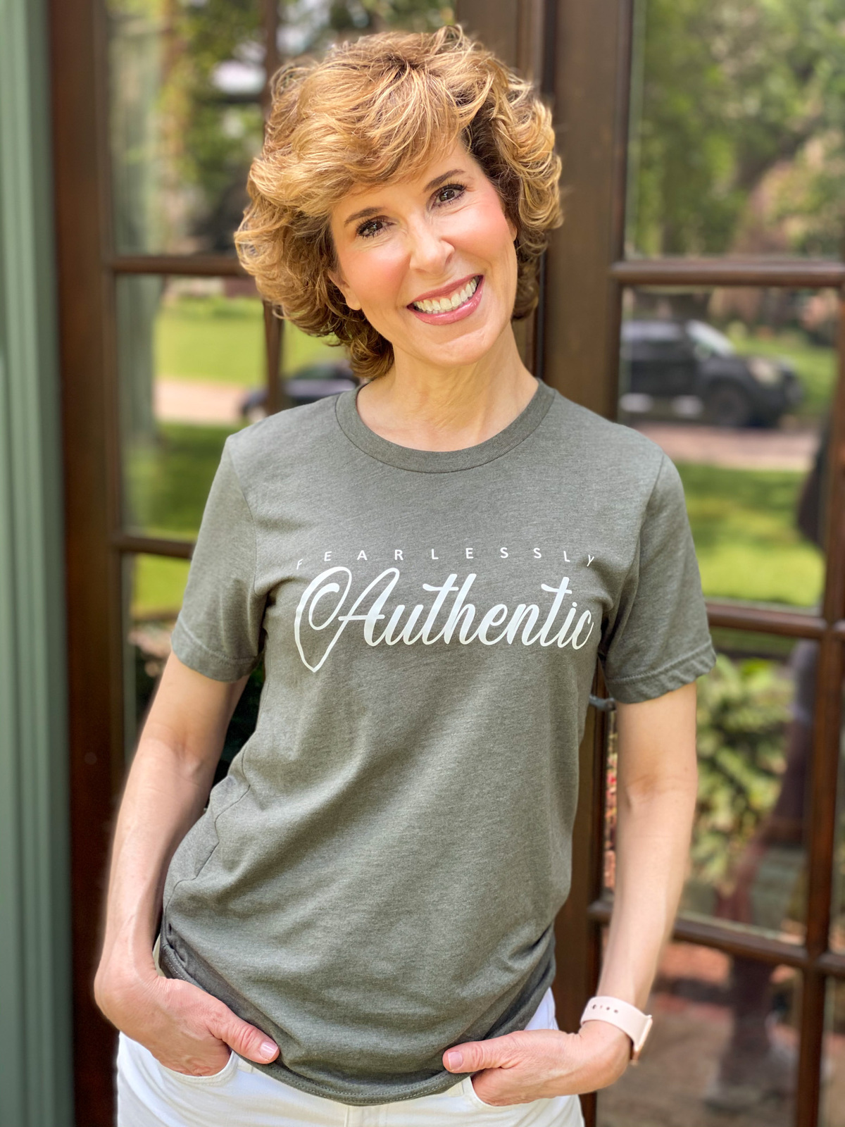 woman over 50 wearing graphic tee standing on porch in front of french doors