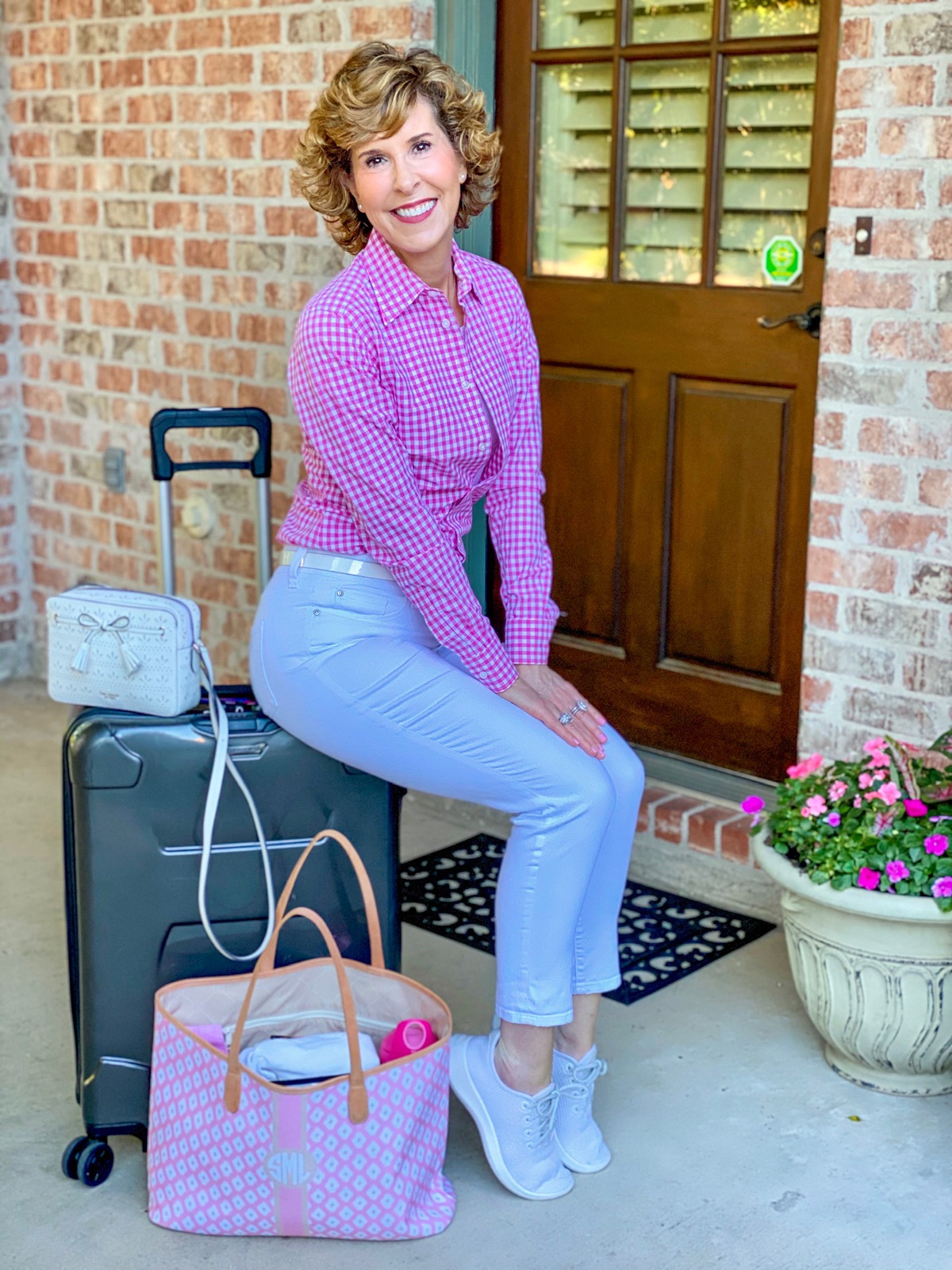 woman in pink gingham shirt sitting on a suitcase