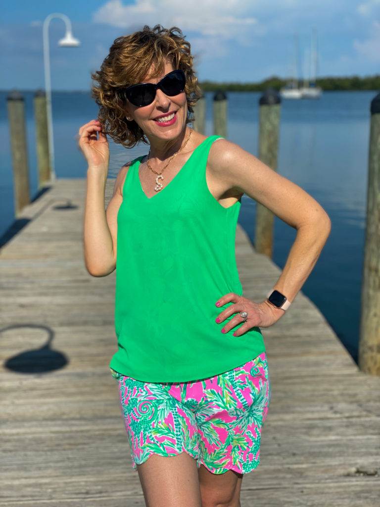 woman wearing green tank top and lilly pulitzer shorts and sunglasses standing on a dock