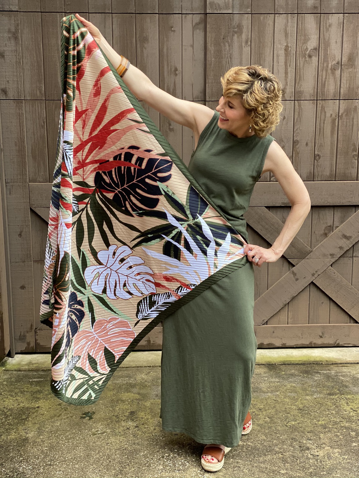 woman holding oversized square palm scarf on the weekend in front of brown wooden wall