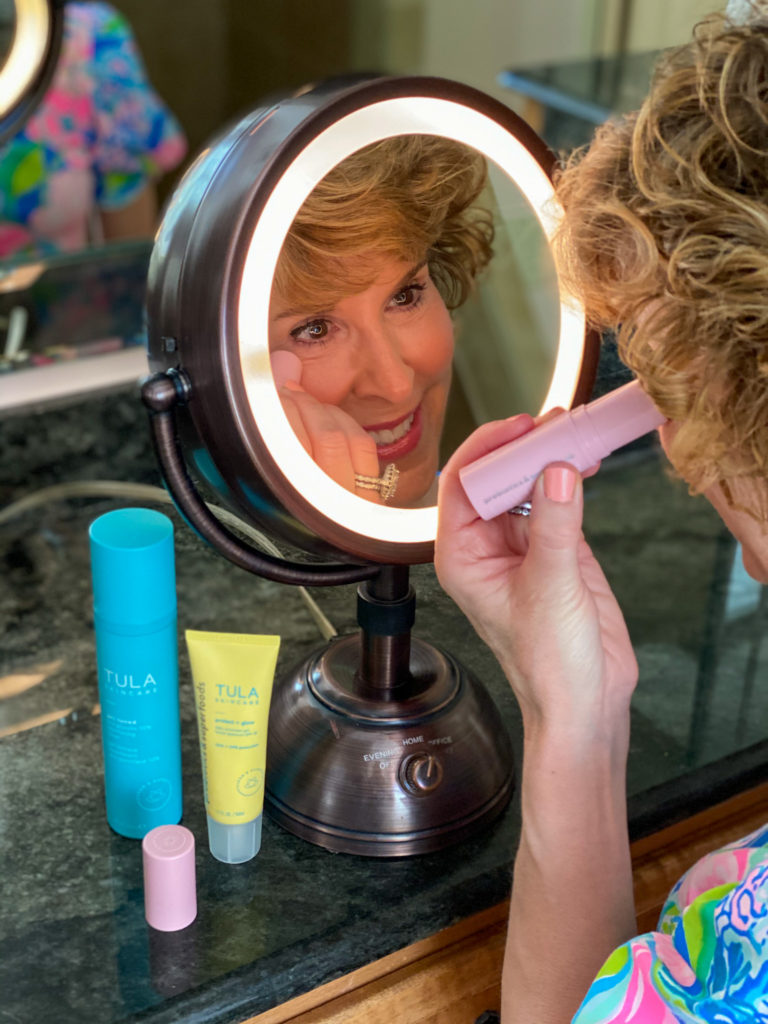 woman applying clean beauty product from pink tube to undereye area