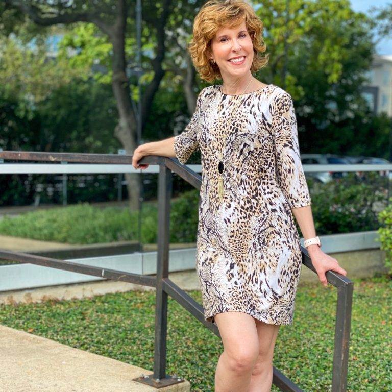 woman in animal print dress leaning against a stair railing in front of an office building