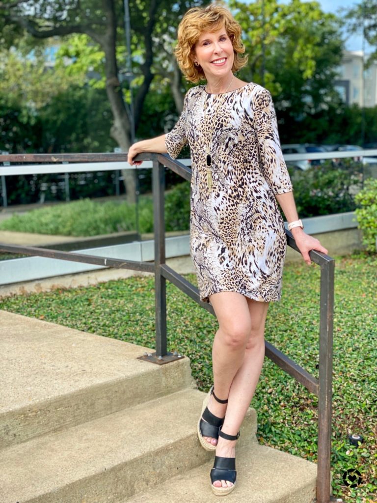 woman in animal print dress leaning against a stair railing in front of an office building