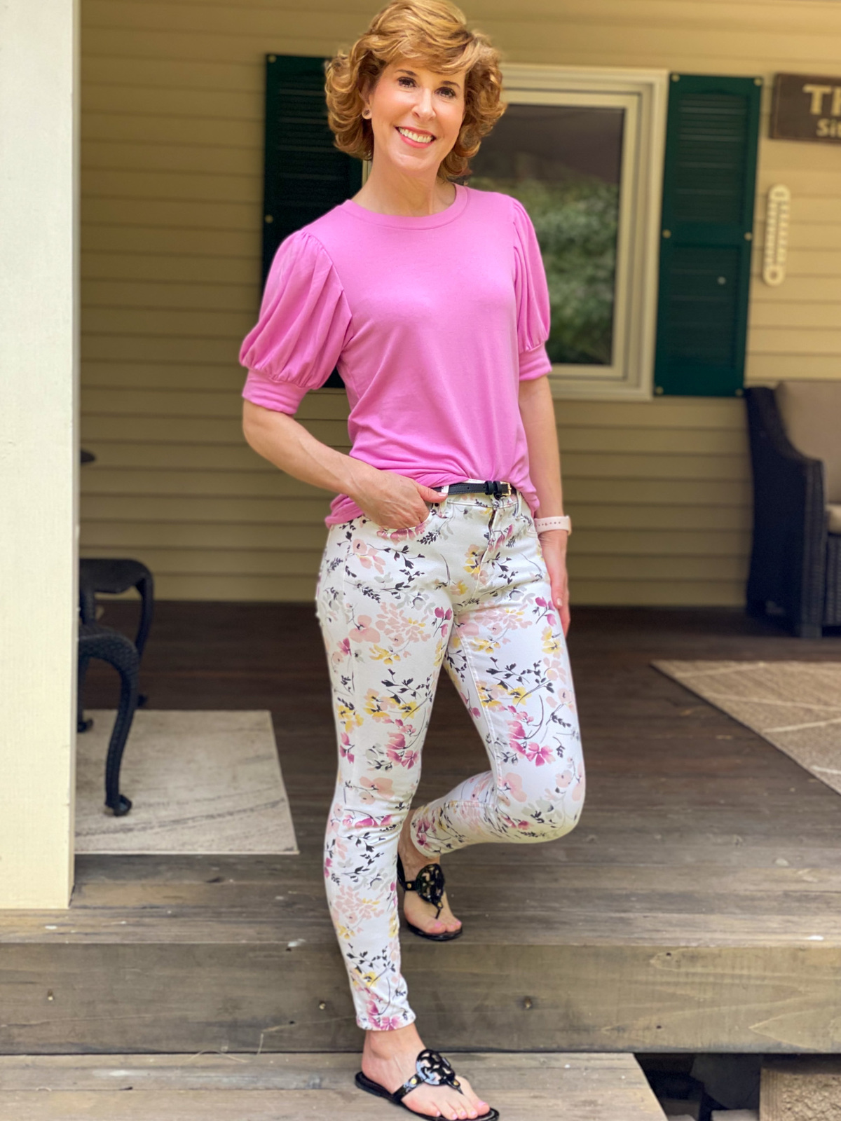 woman wearing pink puffy sleeve tee and floral pants standing on a porch step