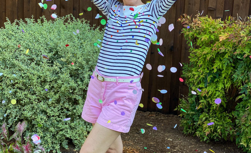 woman wearing pink shorts and striped top throwing confetti in the air