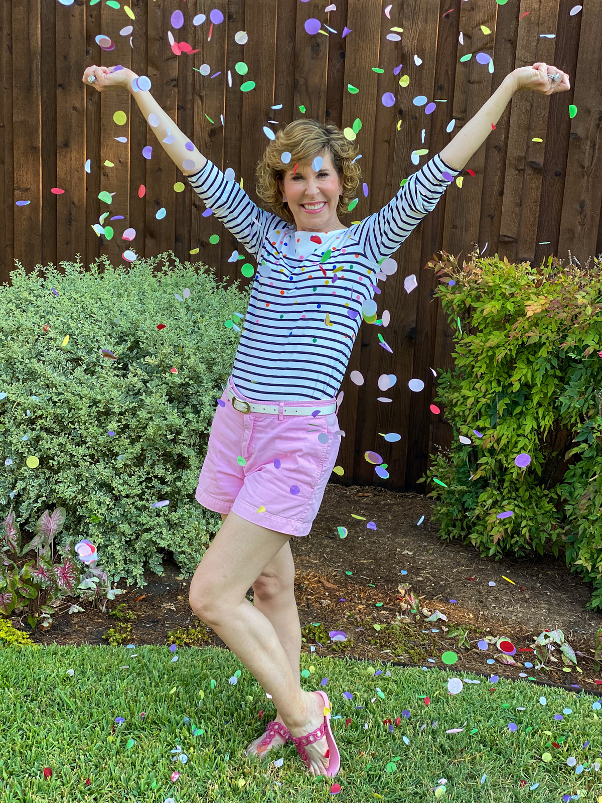 woman wearing pink shorts and striped top throwing confetti in the air