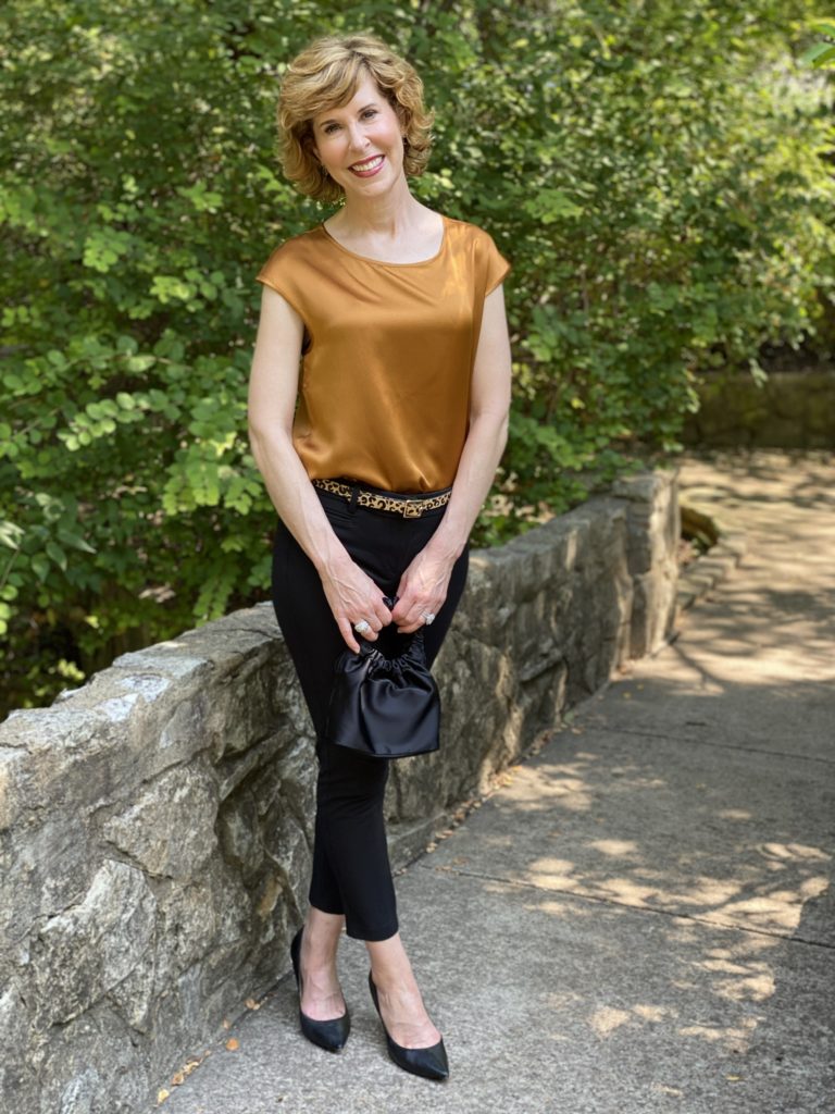 woman wearing lilysilk basic silk tee blak ankle pants leopard print belt black pumps standing on a stone bridge