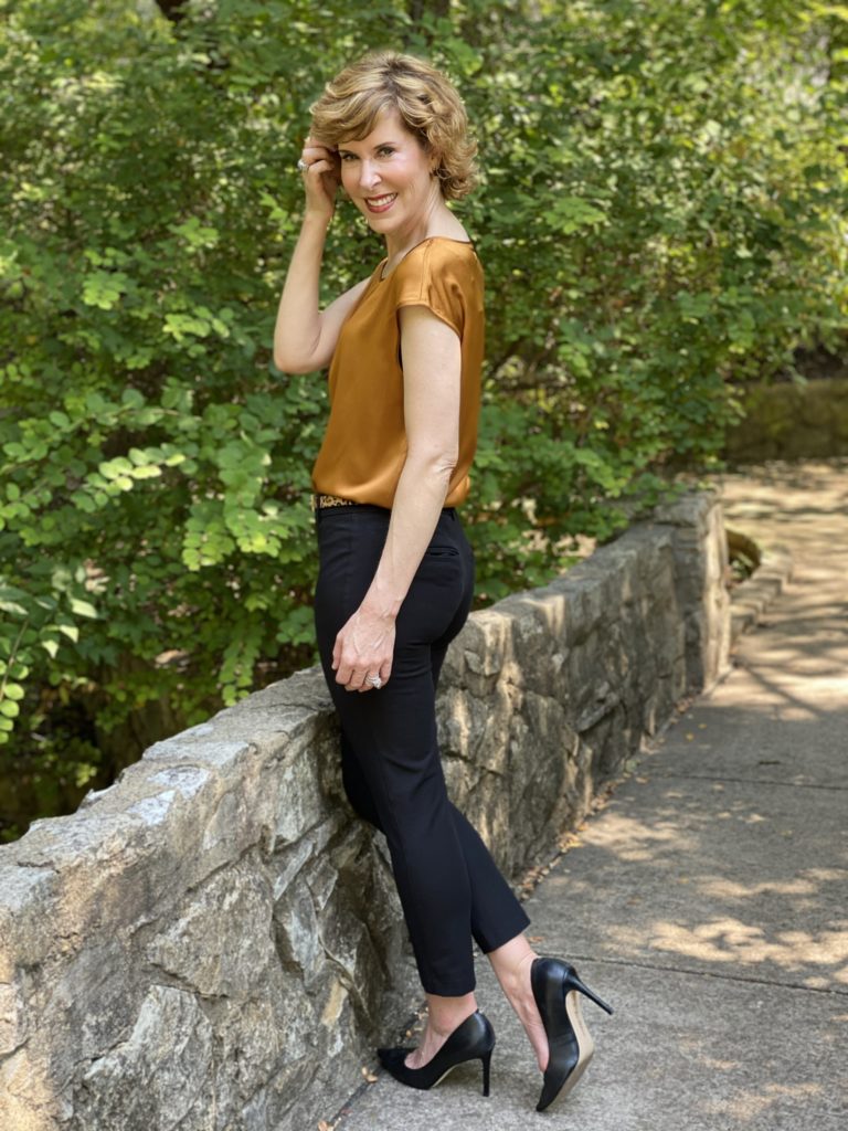 woman wearing lilysilk basic silk tee blak ankle pants leopard print belt black pumps standing on a stone bridge