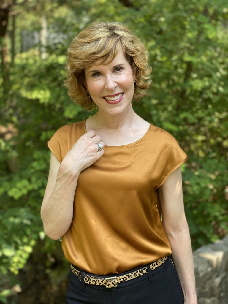 woman wearing lilysilk basic silk tee blak ankle pants leopard print belt black pumps standing on a stone bridge