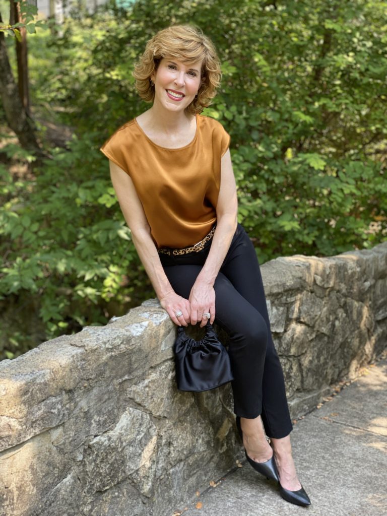 woman wearing lilysilk basic silk tee blak ankle pants leopard print belt black pumps sitting on a stone bridge