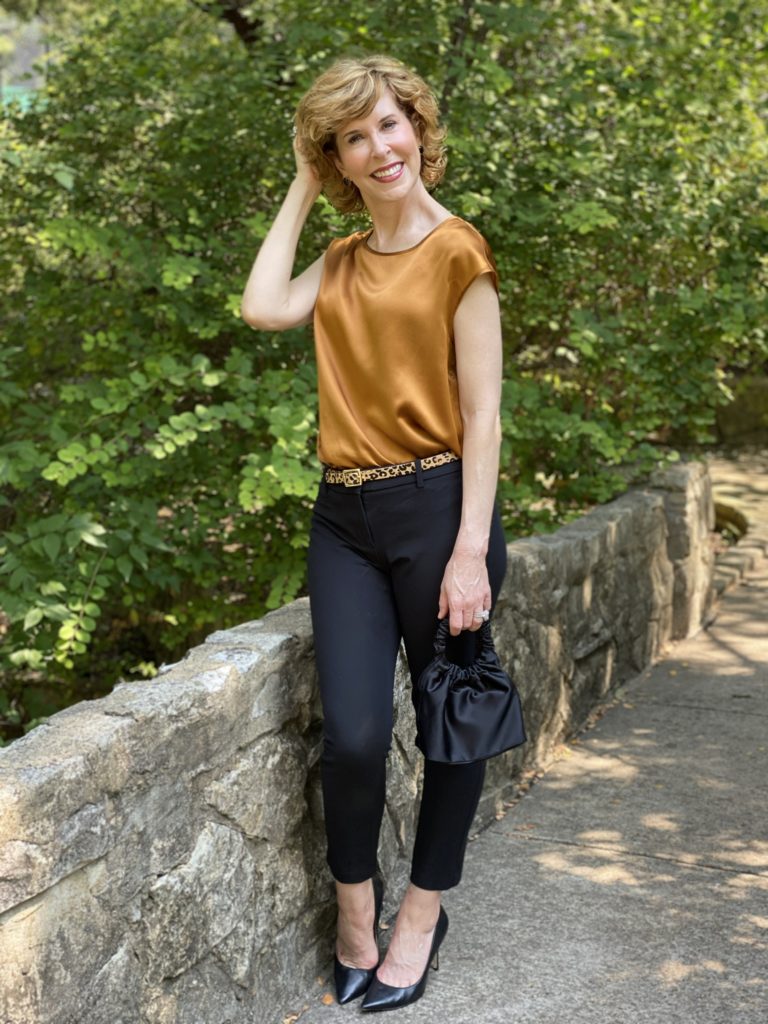 woman wearing lilysilk basic silk tee blak ankle pants leopard print belt black pumps standing on a stone bridge