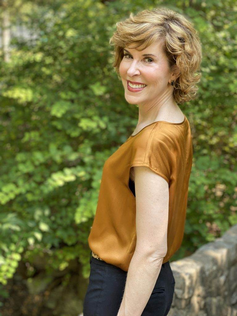 woman wearing lilysilk basic silk tee blak ankle pants leopard print belt black pumps standing on a stone bridge