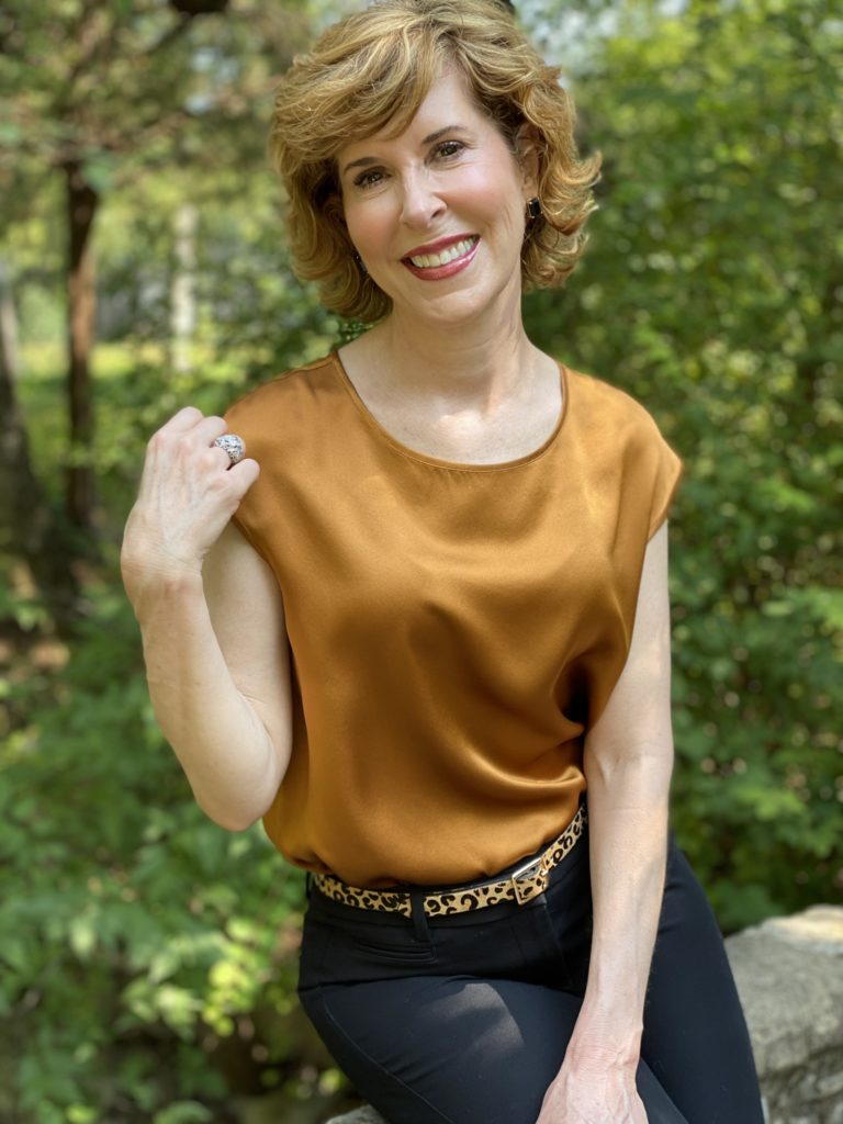 woman wearing lilysilk basic silk tee blak ankle pants leopard print belt black pumps sitting on a stone bridge