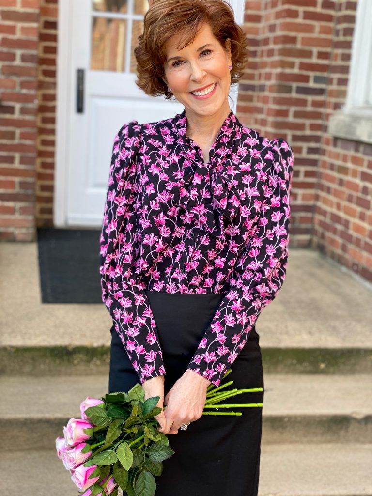 woman wearing a target tie neck blouse with a black pencil skirt holding pink silk roses