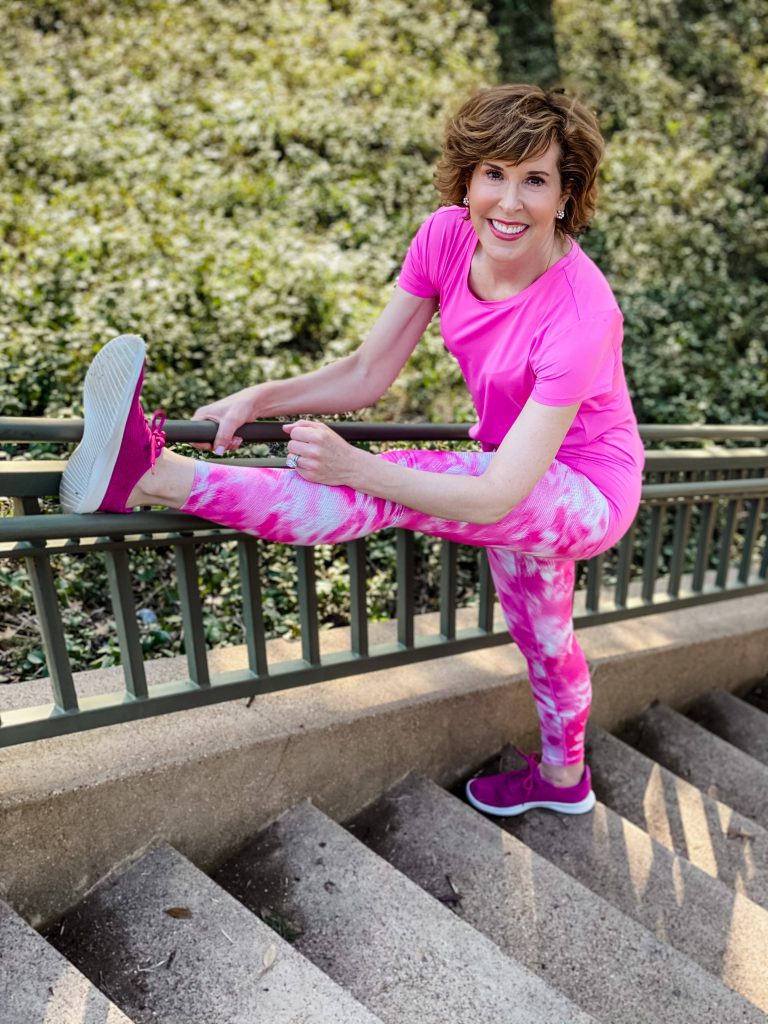 woman aging well over 50 wearing pink zella workout leggings and tee stretching on a staircase