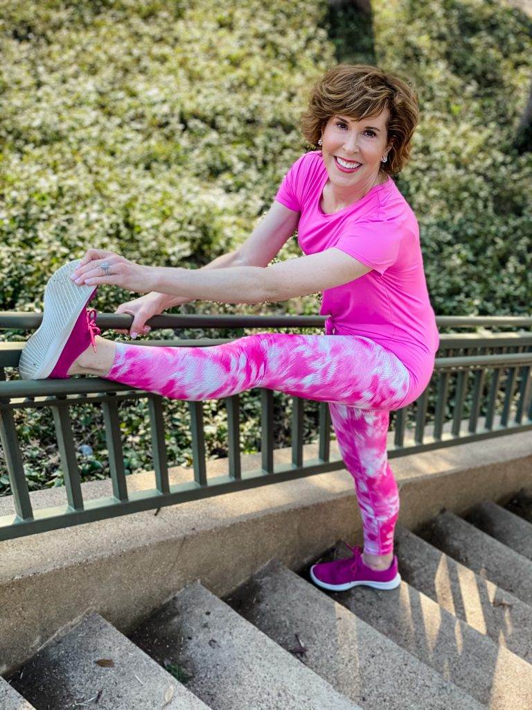 woman aging well over 50 wearing pink zella workout leggings and tee stretching on a staircase