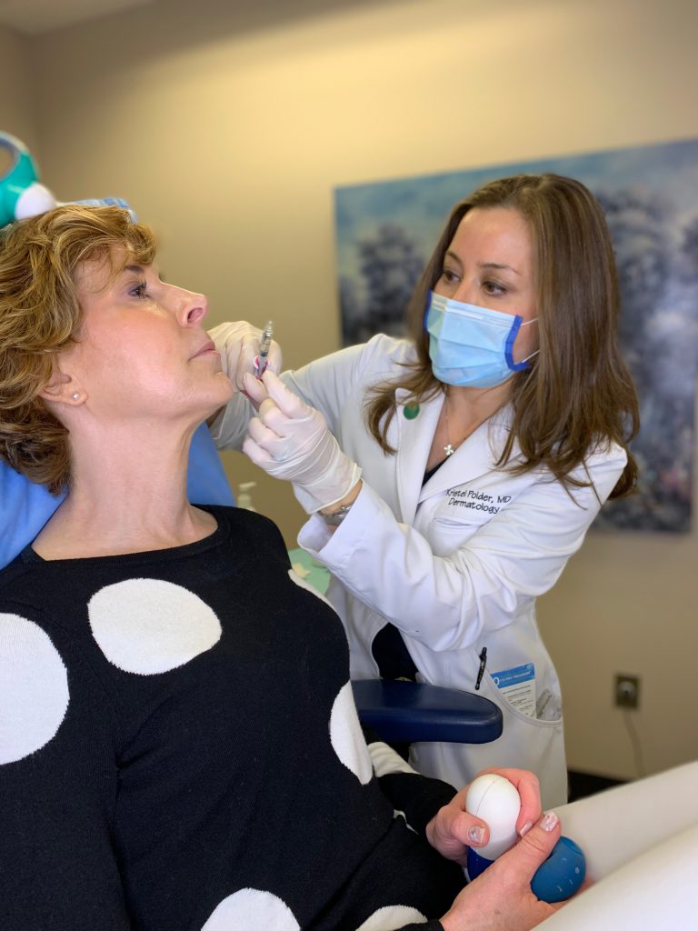 dr kristel polder from the dallas center for dermatology and aesthetics performing dermal fillers on a woman over 50 wearing black and white polka dot sweater